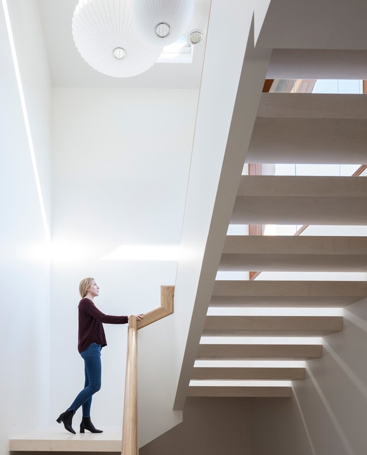 Escalera con luminaria suspendida y pasamanos en madera, lucernario en el techo