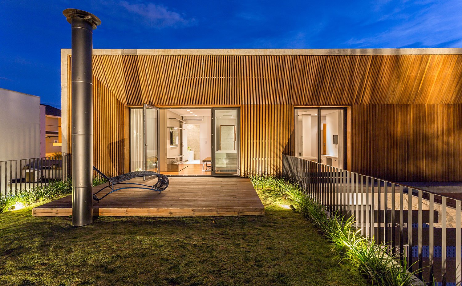 Terraza con plataforma de madera y zona ajardinada, fachada con revestimiento de madera, tubo salida de chimenea