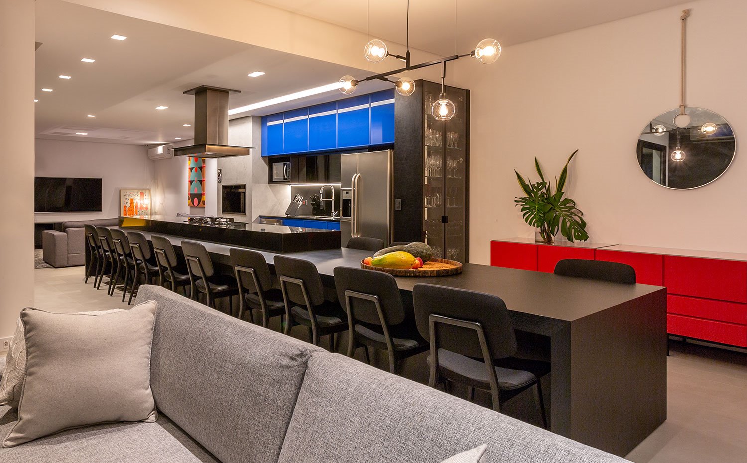 Trasera de sofá junto a cocina abierta con mobiliario lacado en rojo y gran mesa de comedor