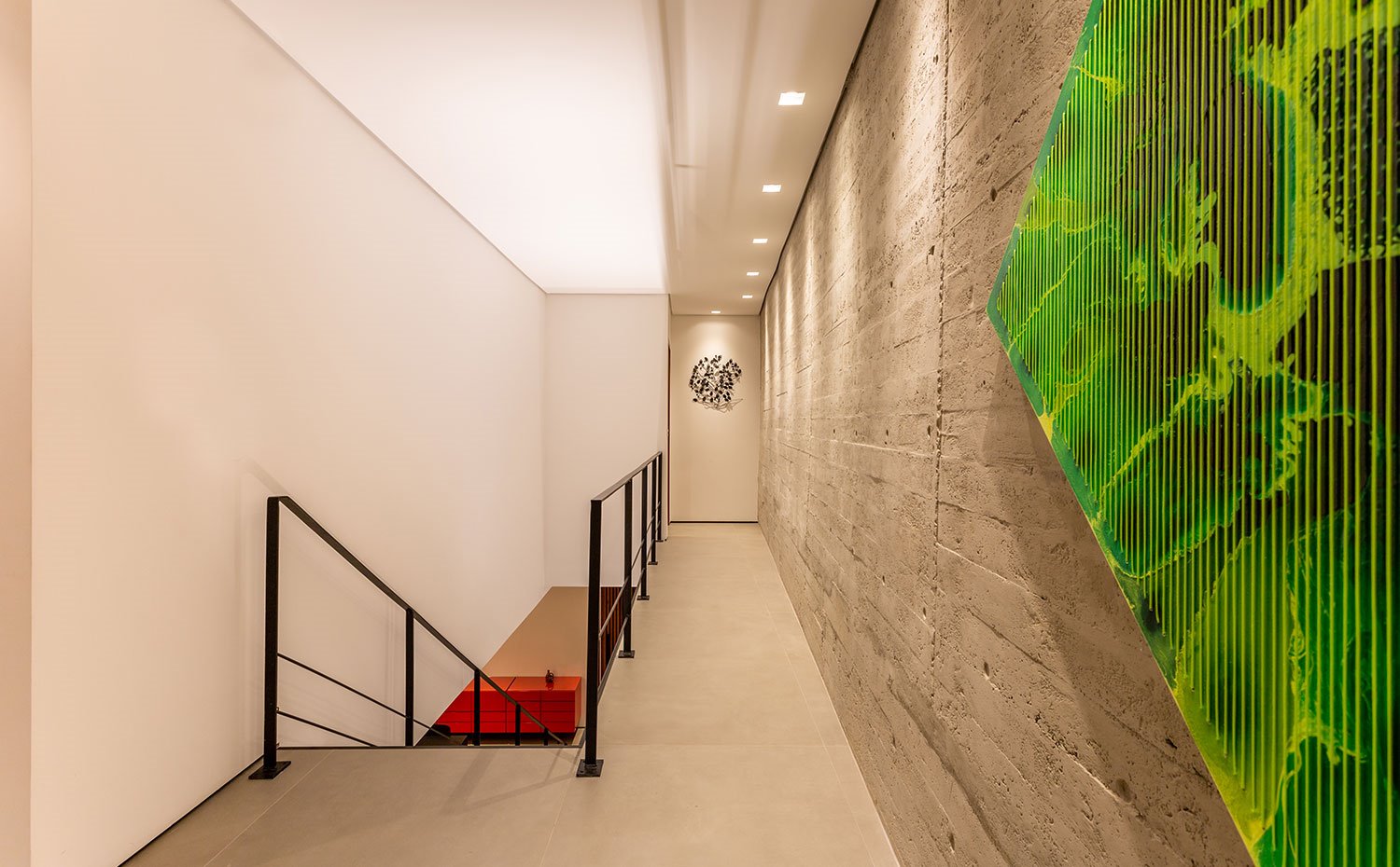 Zona de paso con pavimento porcelánico en gris y pared de hormigón visto, obra de pared en verde