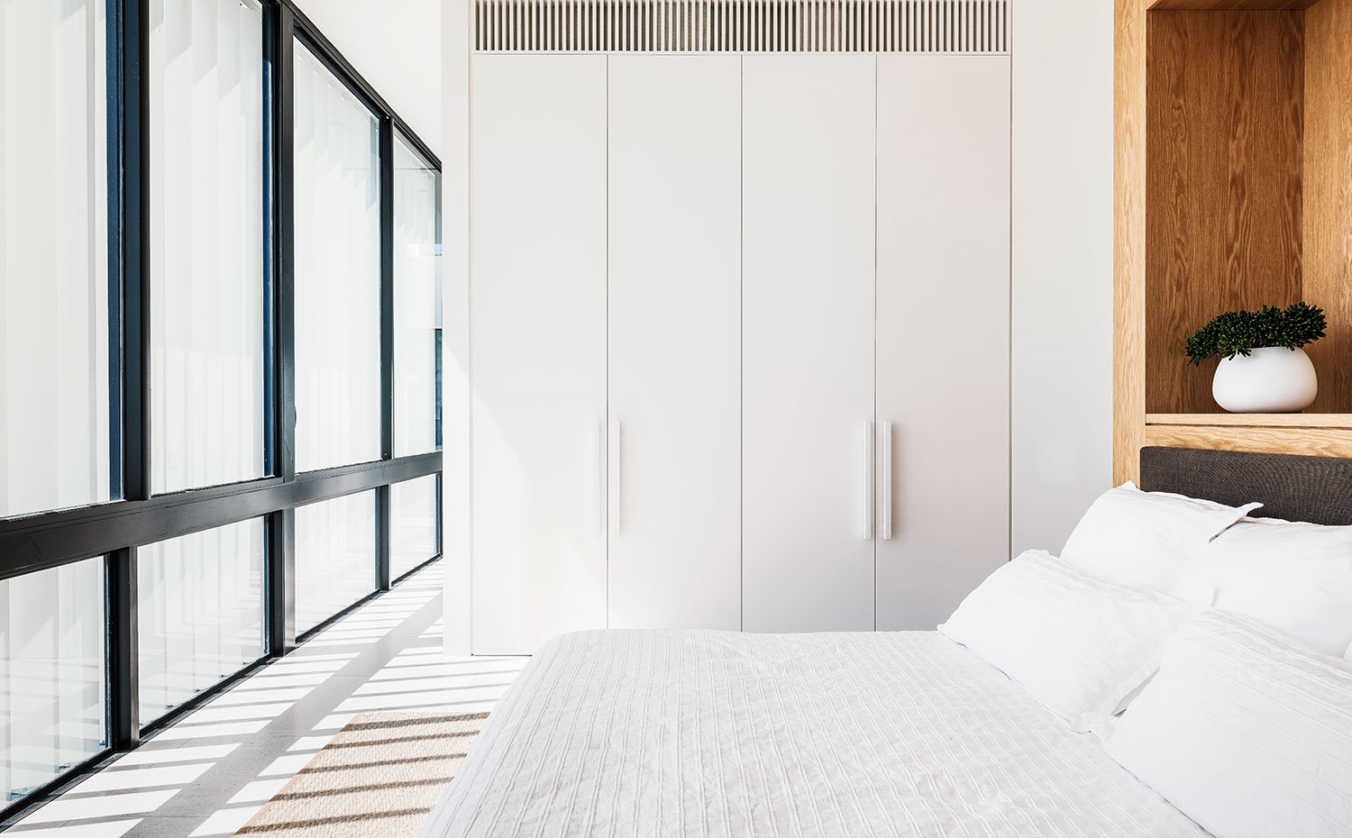 Dormitorio con armarios a modo de separador de ambientes hecho a medida, cabecero en madera natural y frente acristalado 