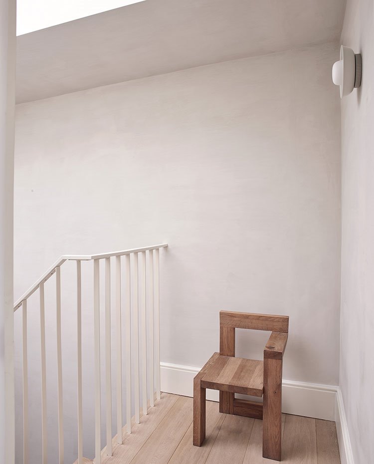 Barandilla de escalera metalizada pintada en blanco, frente a butaca y suelo de madera 