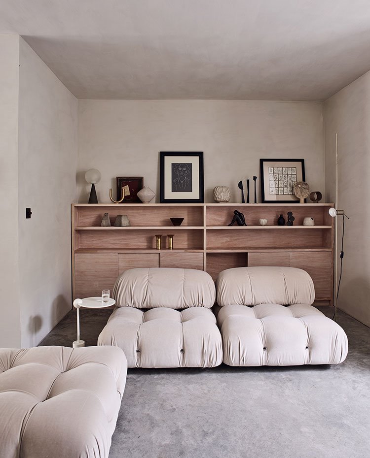 Sillones de formas envolventes en tonos tierra, mesilla auxiliar redonda blanca y mueble con estantes en madera natural 