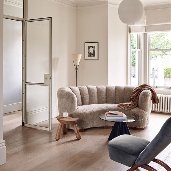 Zona de estar con sofá de pelo en tonos beige, taburete de madra, mesilla de sobre de cristal y butaca en gris
