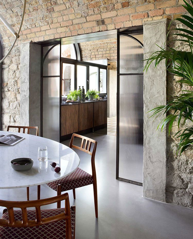 Comedor con mesa circular y sillas en madera y rojo, puerta de cristal ondulado hacia cocina