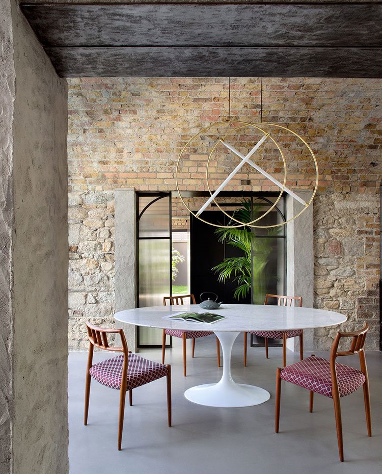 comedor con paredes de piedra y ladrillo visto, mesa de centro circular en blanco y sillas de madera tapizadas en rojo
