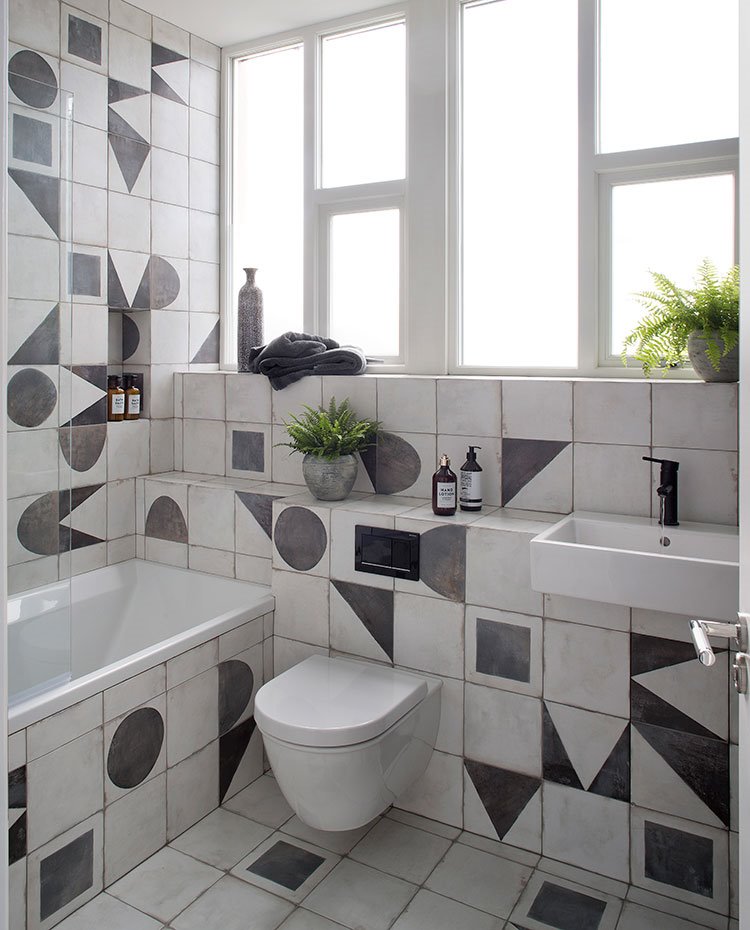 Cuarto de baño con inodoro y lavamanos suspendido, baldosas con motivos geométricos en blanco y negro