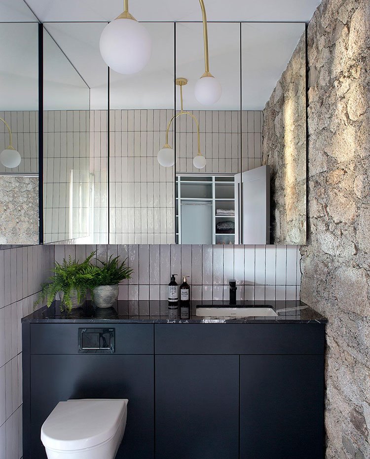 Cuarto de baño con mueble bajo en negro, con inodoro integrado, baldosas vintage con frente de pared de piedra vista y luminarias con pantallas esféricas