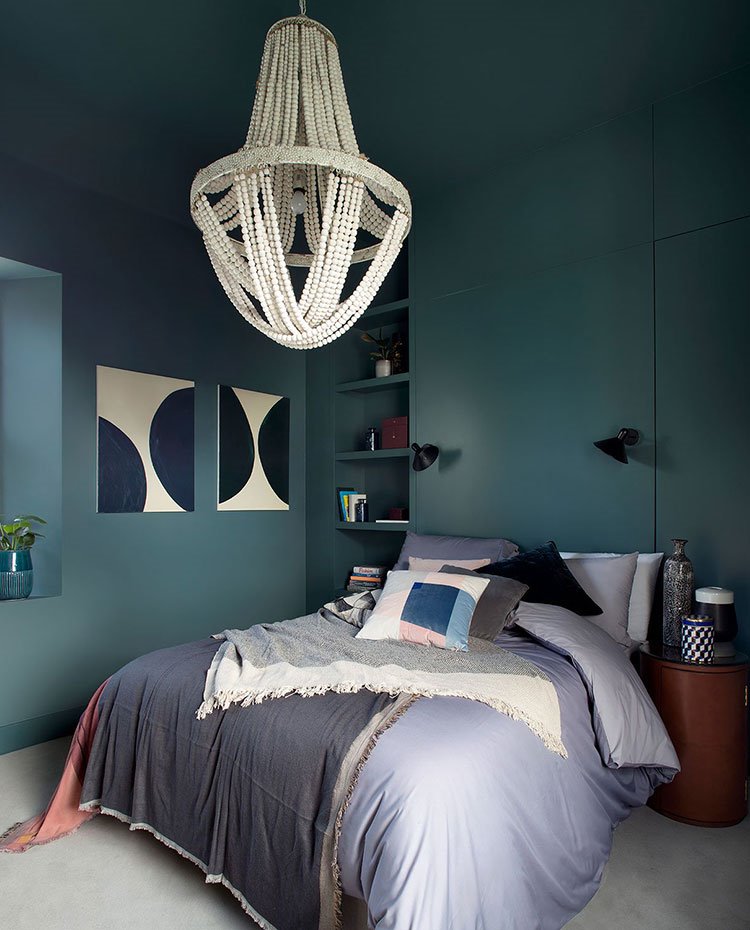 Dormitorio con pared y techo en tonos azul verdoso, luminaria suspendida a modo de piedrecitas, cuadros de motivos geométricos blancos y negros, apliques en negro