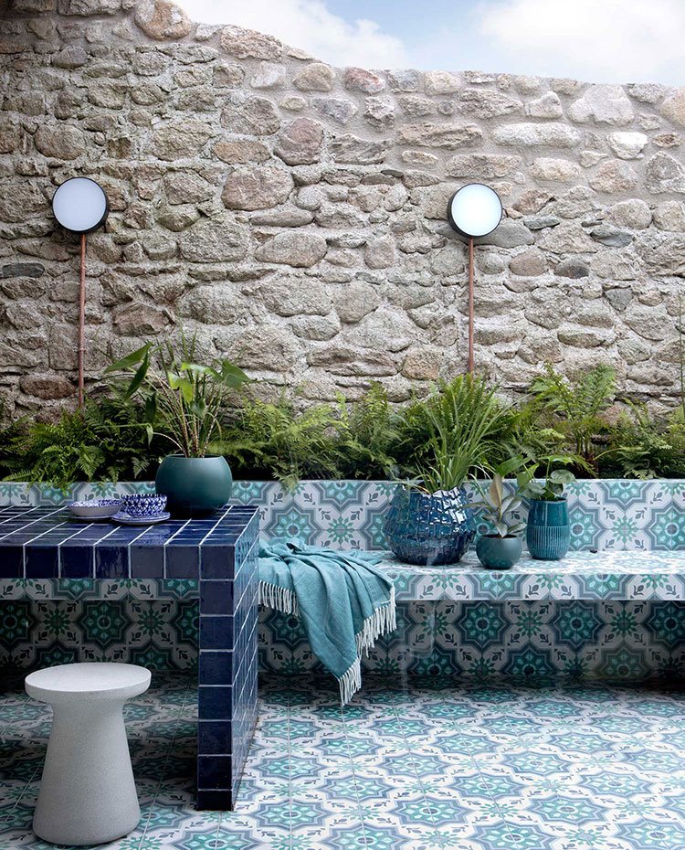 Jardín exterior con jardinera tras bancada de obra, revestida con el mismo gres del suelo, mesa revestida de gres azul y taburete gris