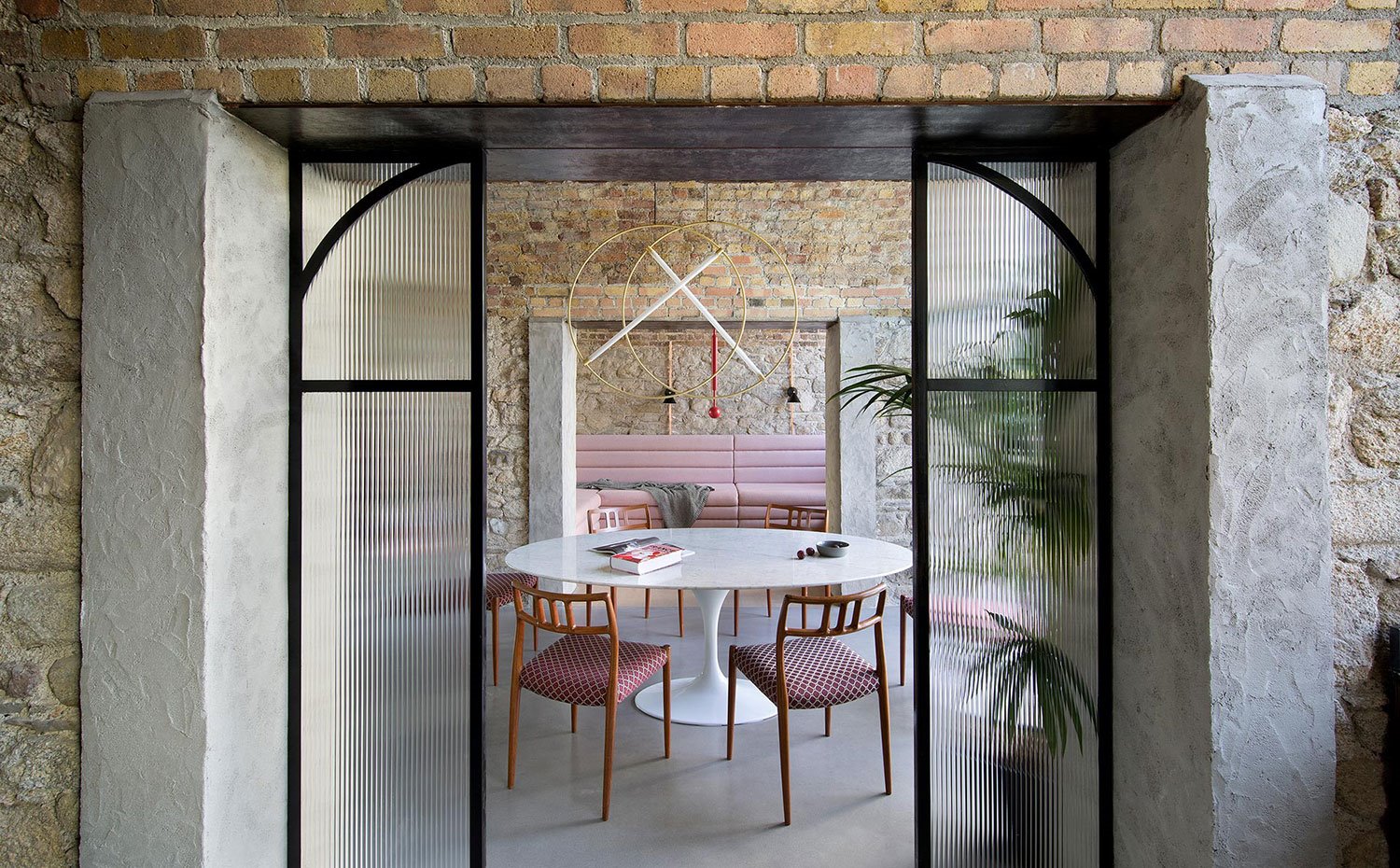 Puerta acristalada con perfilería en negro hacia comedor con mesa blanca y sillas en rojo y salón, con sofá en rosa