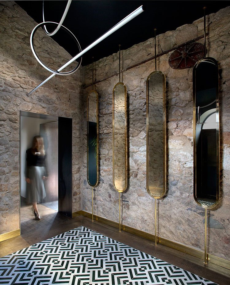 Zona de paso con varios espejos dispuestos frente a pared de piedra, anclados en techo y suelo