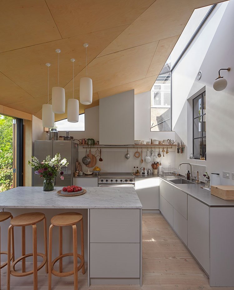 Amplia cocina abierta con lucernarios y aperturas al exterior y cubierta irregular revestida de madera