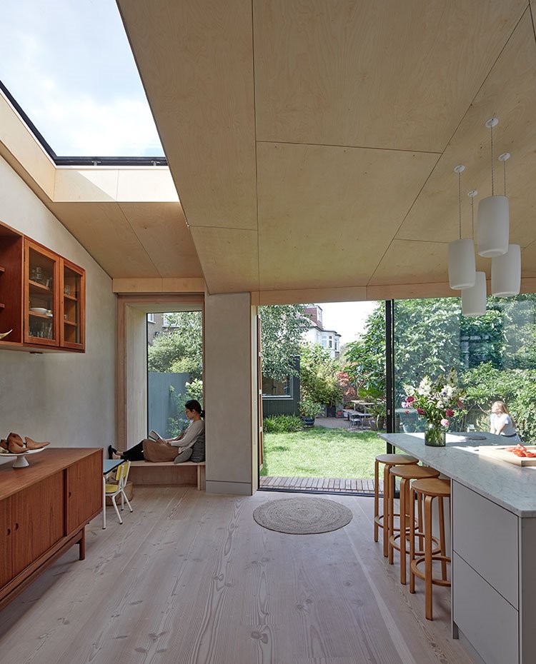 Zona de día junto a cocina abierta y exterior, con lucernario junto a cubierta de madera