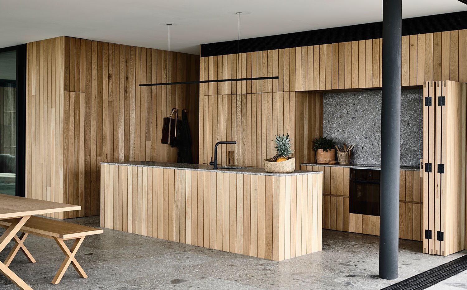 Cocina revestida de listones de madera, zona de cocción con frente plegable, mesa y banco de madera