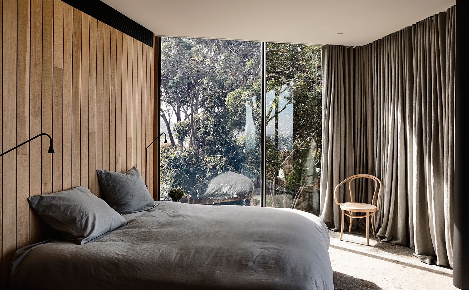Dormitorio con cerramientos transparentes al exterior y cortinas en gris para aislar del exterior