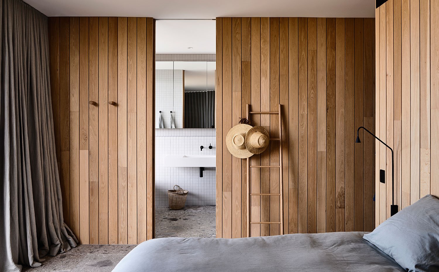 Dormitorio con cuarto de baño integrado con cortinas y ropa de cama en gris