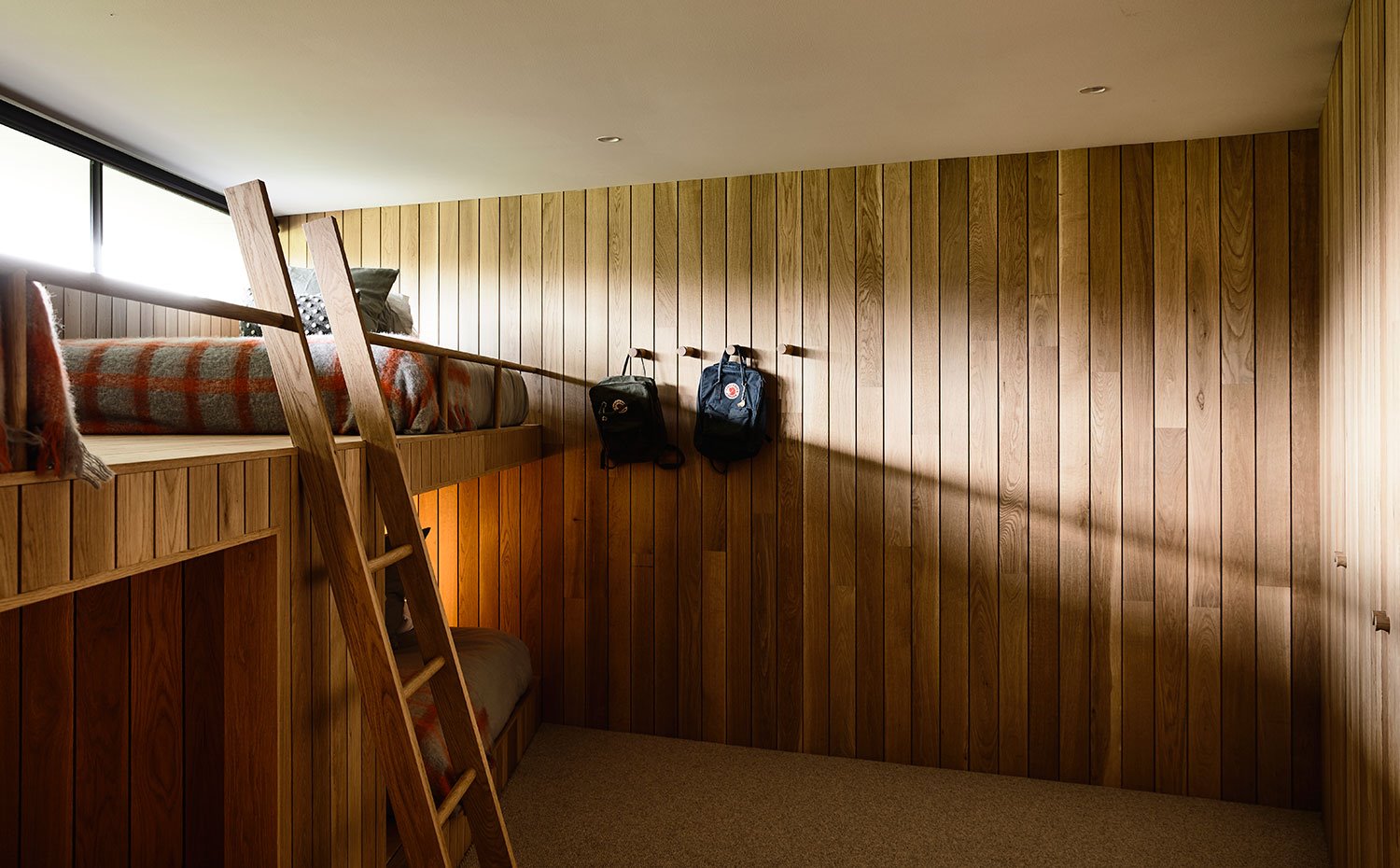 Dormitorio infantil con litera y revestimiento alistonado en madera, ventanas apaisadas en la parte superior