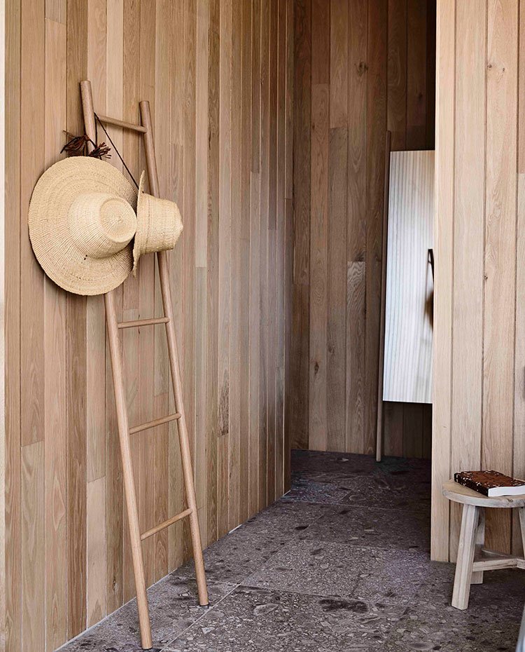 Paredes paneladas de madera, toallero de madera, sombreros de paja, espejo de pie, taburete de madera