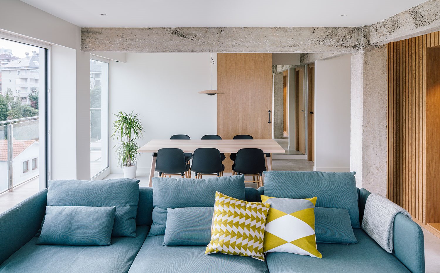 Salón con sofá azúl grisáceo, cojines con motivos gráficos y mesa de comedor de madera con sillas en negro
