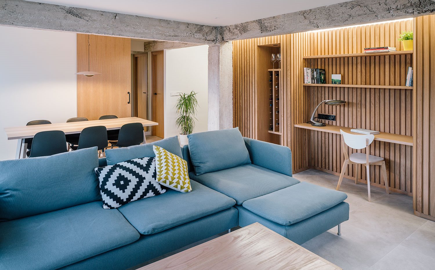 Sofá en azul, revestimiento en madera alistonada, vigas y columnas de hormigón