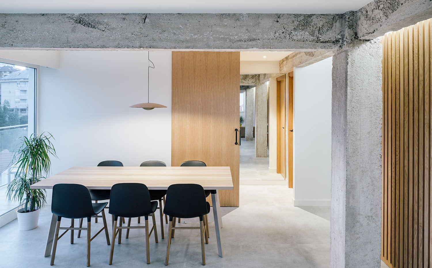Zona comedor con mesa de centro en madera, sillas negras, luminaria suspendida con detalles en latón y puerta corredera 