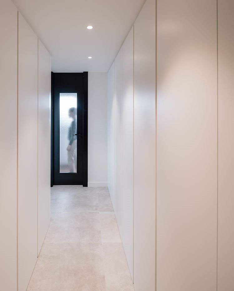Zona de paso con armarios integrados en paredes, sin tiradores, puerta parcialmente de cristal en negro