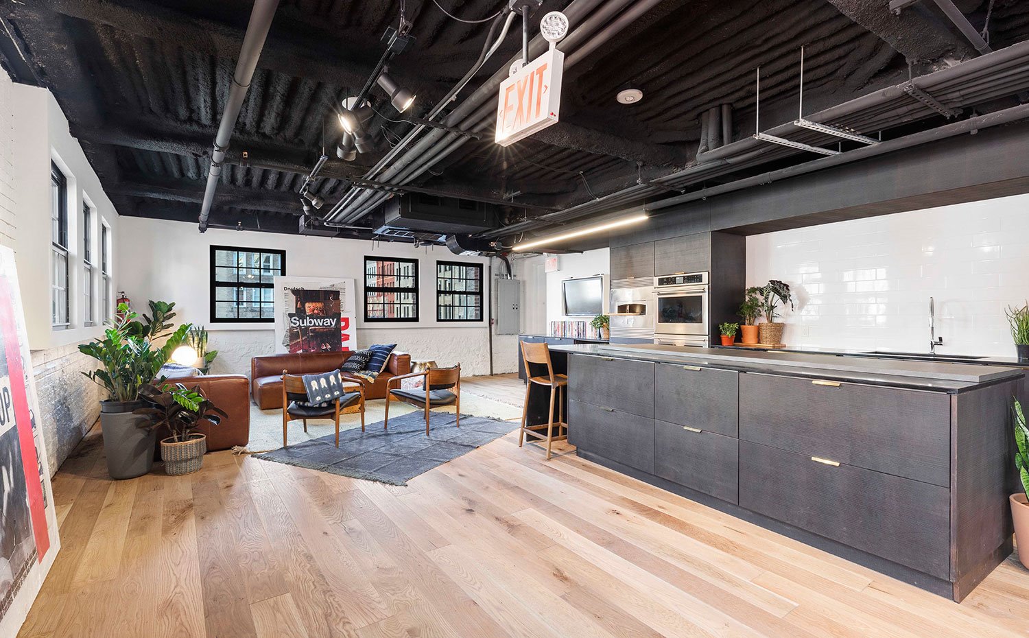 Espacio de coworking con sofás de piel marrón y cocina con isla de acero