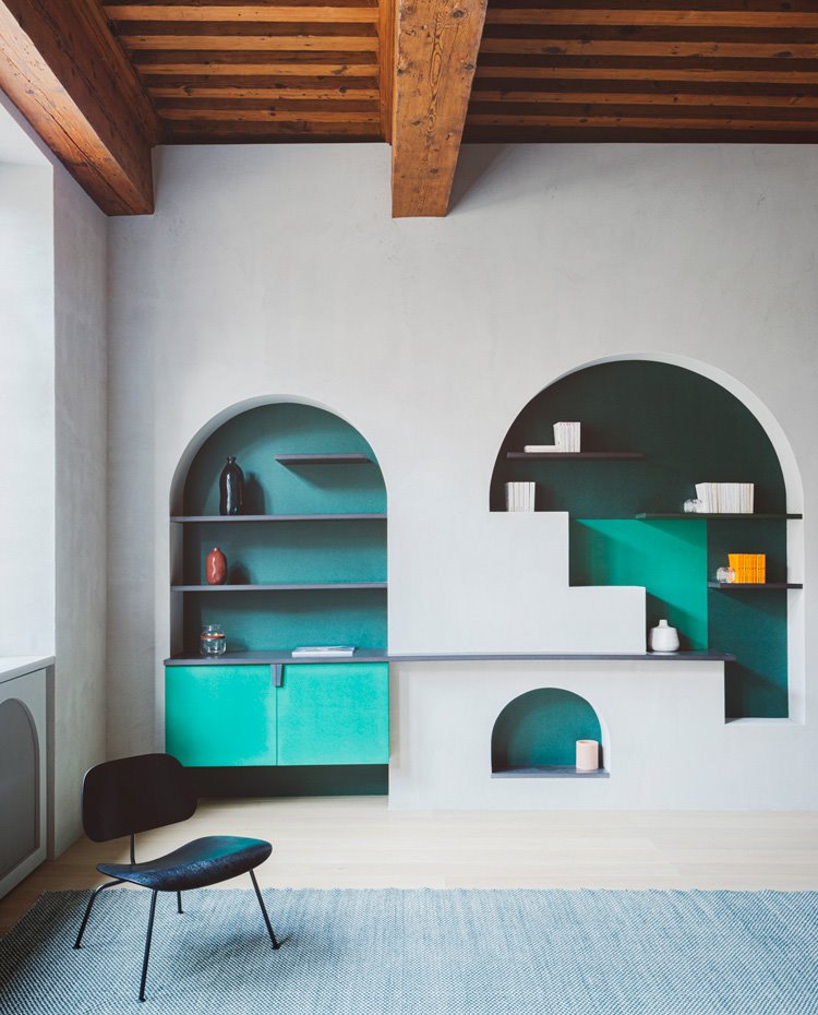 Zona de estar con techos de amdera, huecos en pared de forma abovedada con estantes en negro y módulos en verde