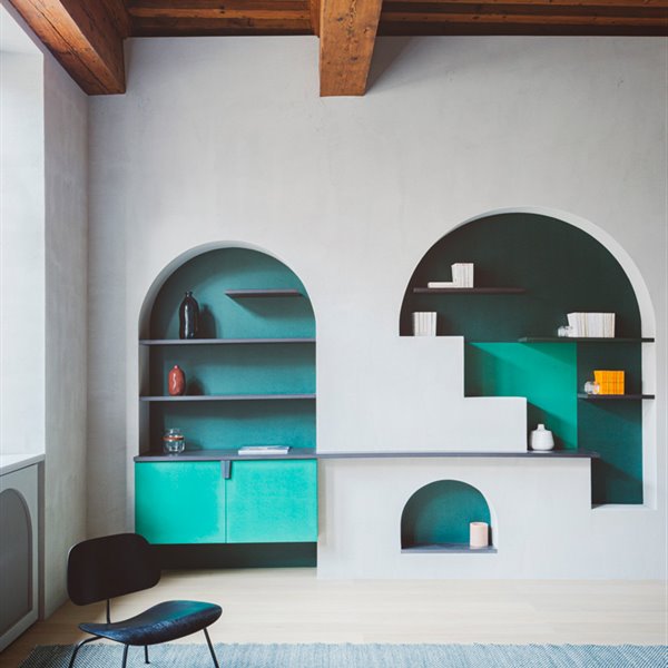 Zona de estar con techos de amdera, huecos en pared de forma abovedada con estantes en negro y módulos en verde
