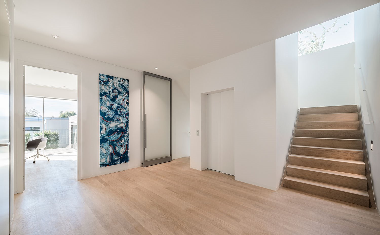 Zona diáfana con pavimento de madera, puertas abatibles en cristal y madera, zona de estudio 