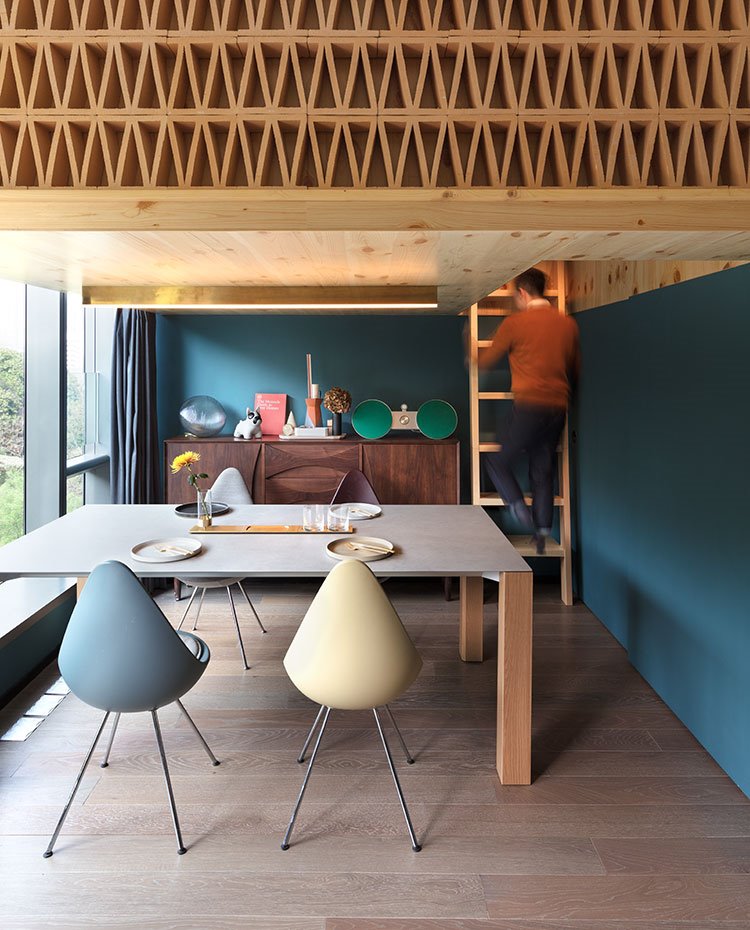 Mesa comedor con sillas de diferentes colores, suelo de madera y escalera a altillo
