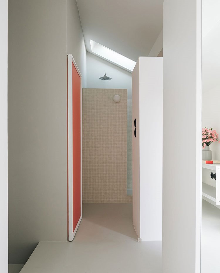 Acceso a cuarto de baño revestido de grasite en crudo y puerta en tonos teja, lucernario bajo cubierta