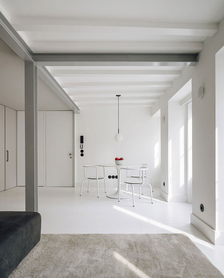 Comedor con mesa, sillas, paredes y suelo en blanco, alfombra en gris claro y sofá en gris oscuro