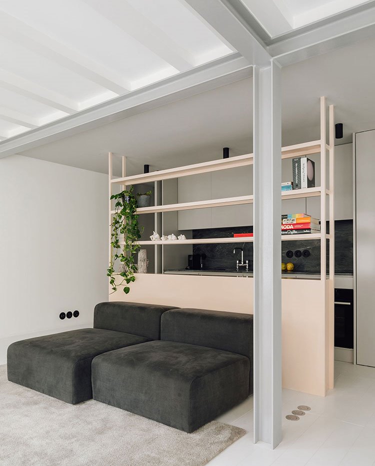 Sofá modular en gris oscuro apoyados sobre estrucutra divisoria, detras la cocina