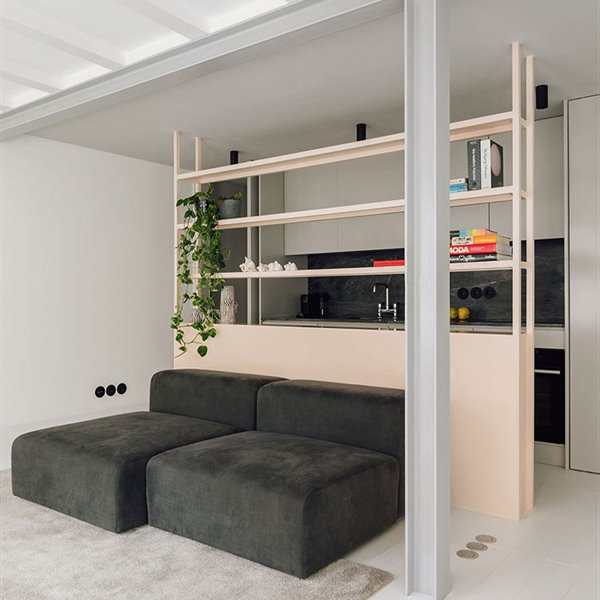 Sofá modular en gris oscuro apoyados sobre estrucutra divisoria, detras la cocina