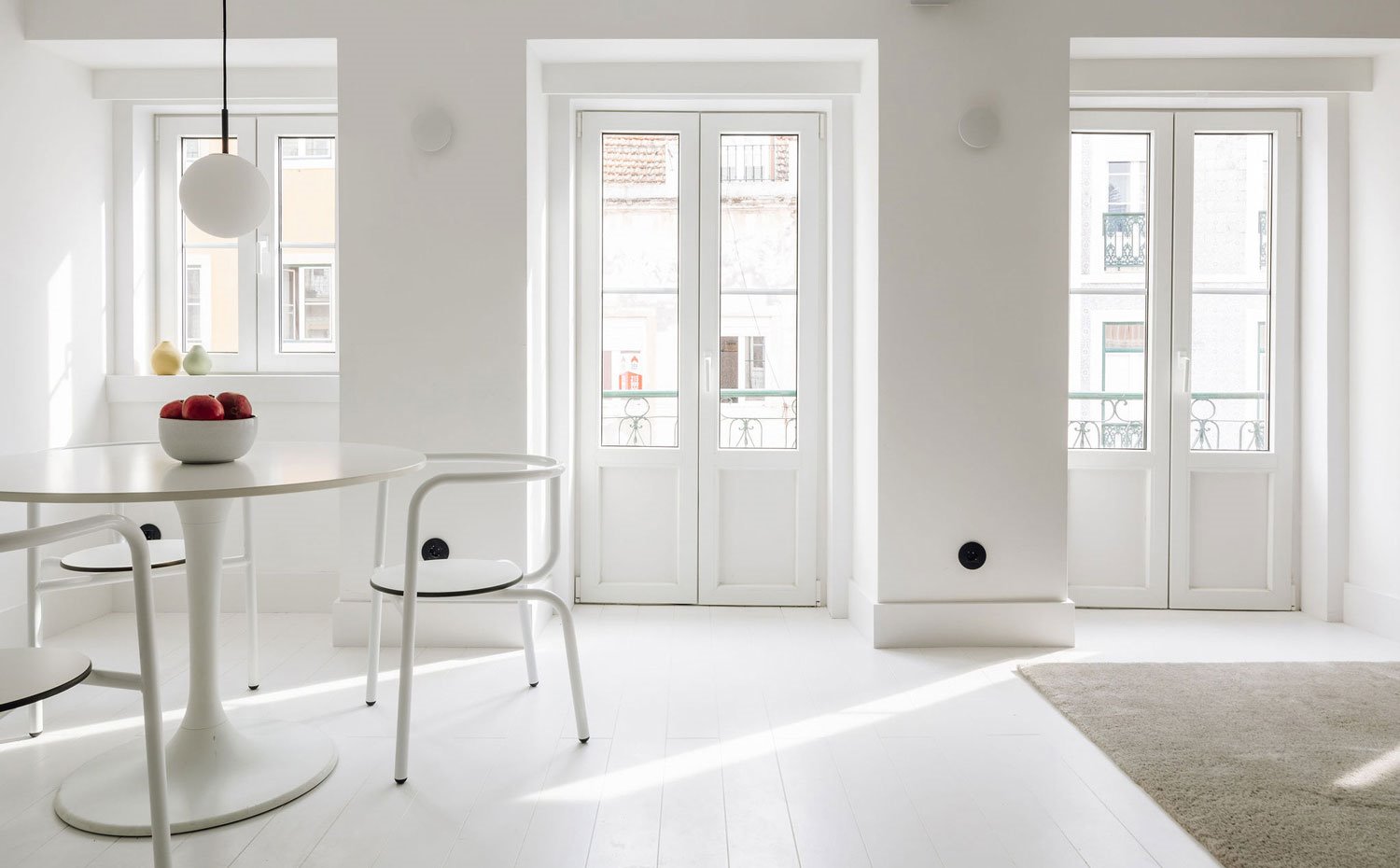 Ventana y balcones hacia exterior vivineda, suelo de madera pintada blanca y mobiliario en blanco