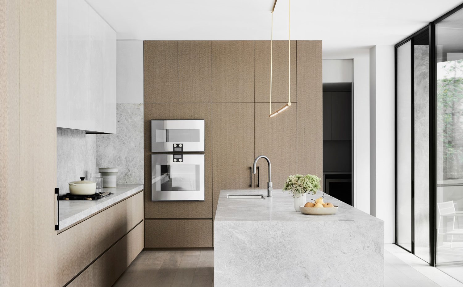 Mobiliario de cocina en madera natural con encimera de piel y armarios superiores en blanco
