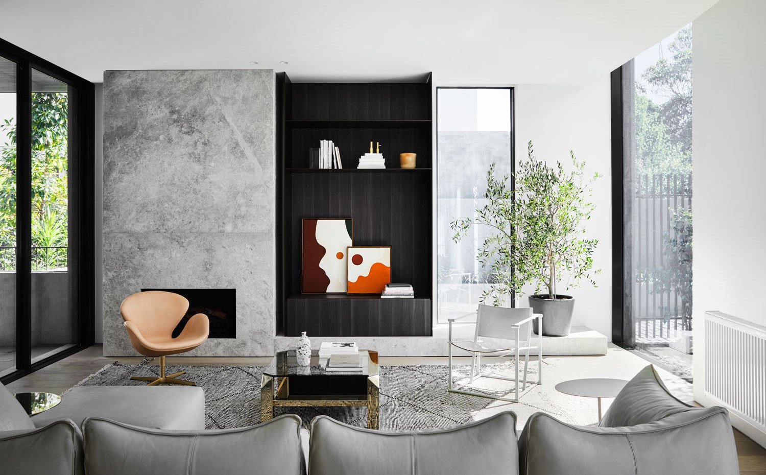 Salón con sofá en gris, chimenea revestida de piedra gris, estantería de madera oscura, butacas en marrón y blanco
