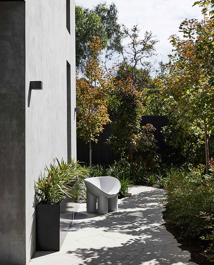 Zona ajardinada junto a fachada de la vivienda con asiento en blanco y gris