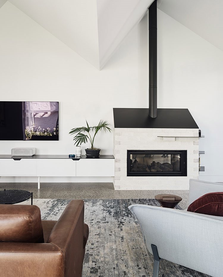 Chimenea de madera junto a mueble bajo en blanco con sobre en negro, alfombra en gris, sofá marrón