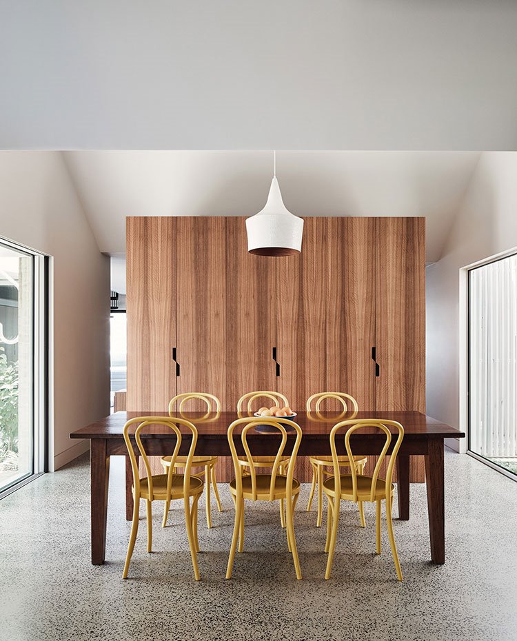 Comedor con mesa en madera y sillas en amarillo, armarios de madera y luminaria suspendida en blanco