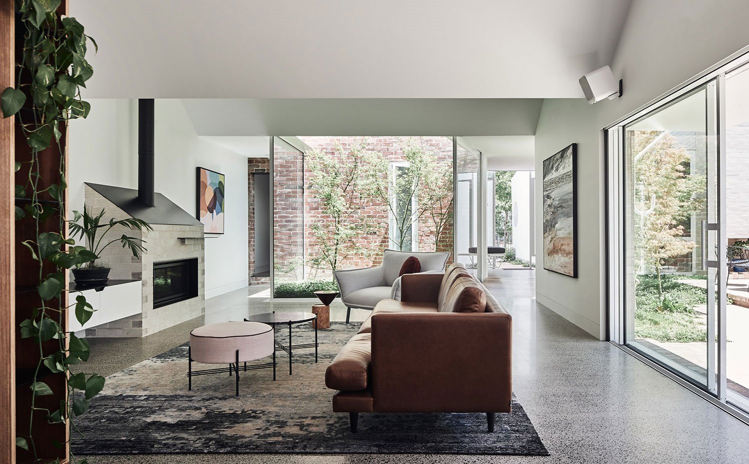 Salón con sofá en marrón, alfombra tornasolada en azul y grisl, pouf en rosa y chimenea