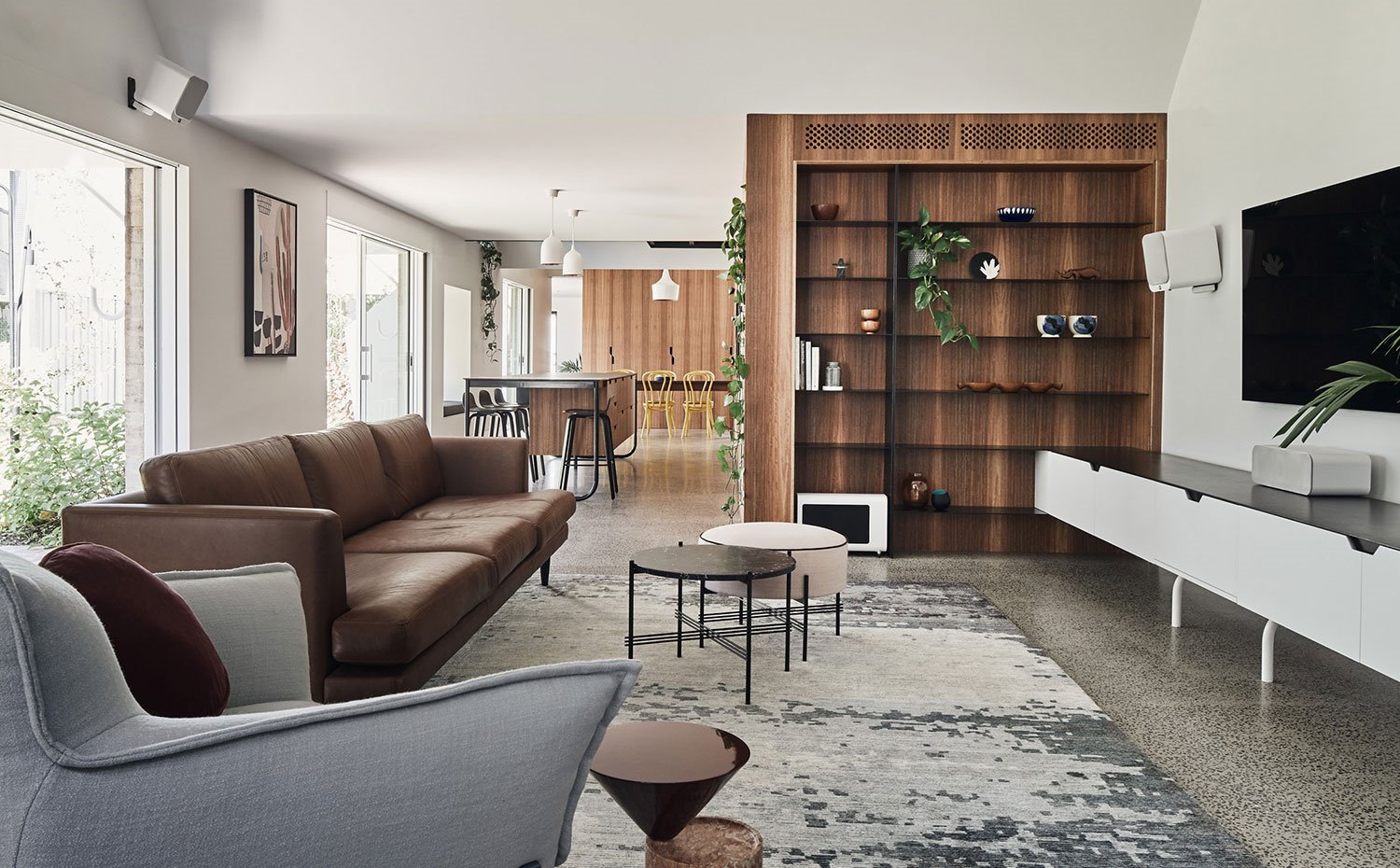 Salón con sofá marrón, butaca en gris, mueble bajo televisor en blanco, estantería en madera