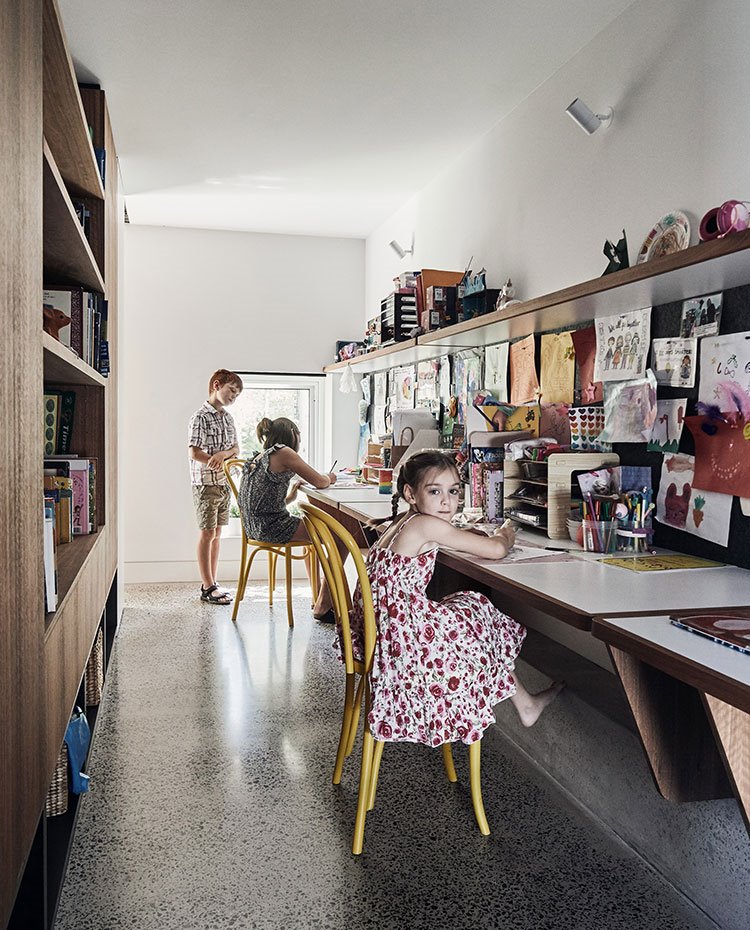 Zona de trabajo infantil con mesa alargada y estantería superior