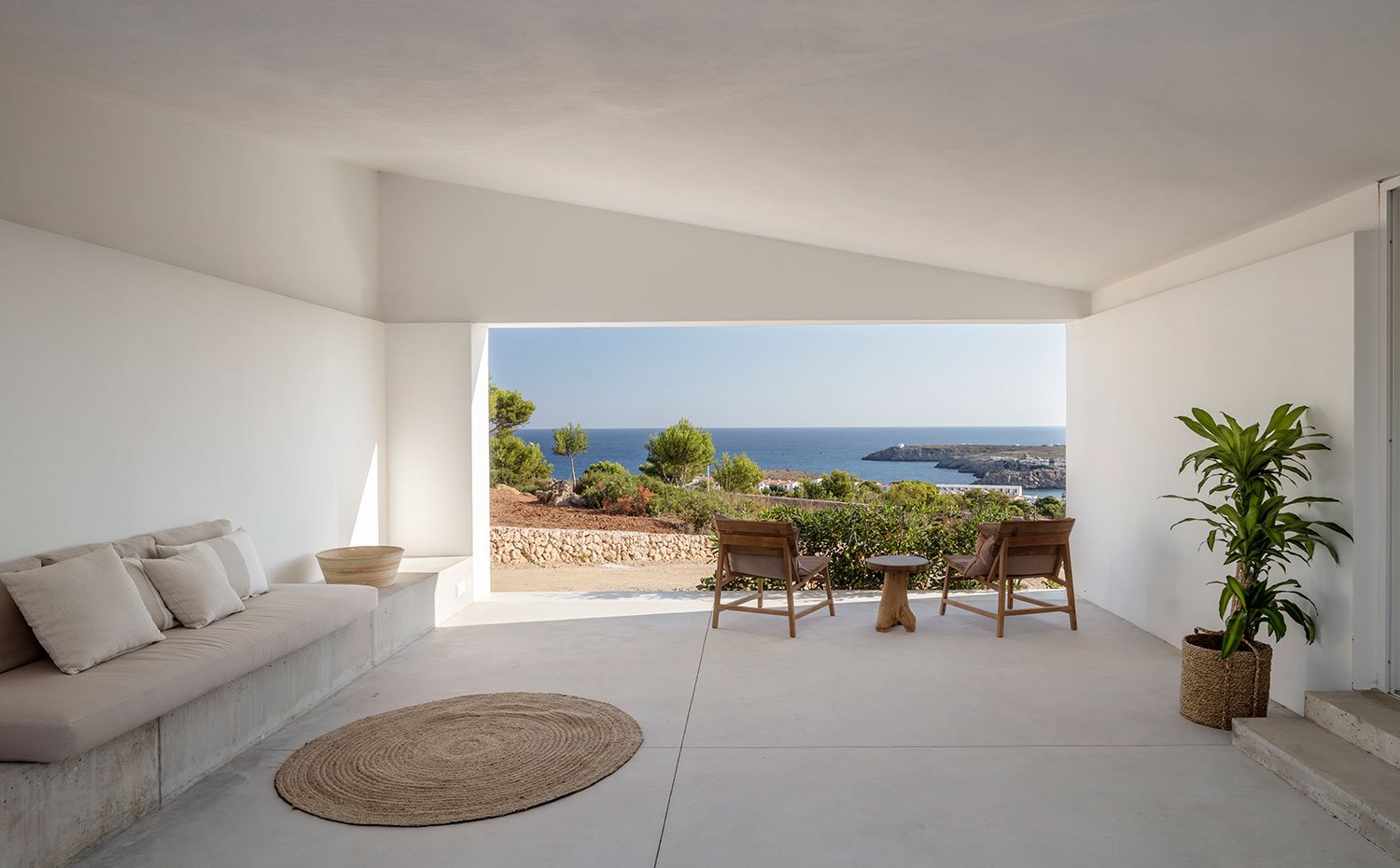 Porche cubierto con sofá de obra, alfombra circular de fibra natural, butacas y mesa de madera