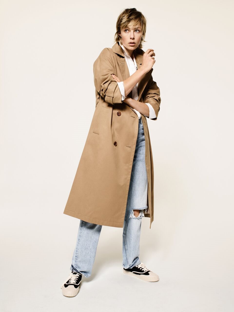 Una clásica gabardina, una camisa blanca esencial, unos vaqueros rotos, unas zapatillas de aire vintage. No se necesita más para conseguir un look por encima de las tendencias.
