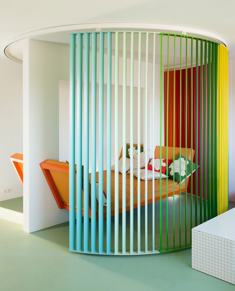 Aristas del biombo corredero con guías de formato circular en una secuencia de colores entorno al sofá-cama naranja