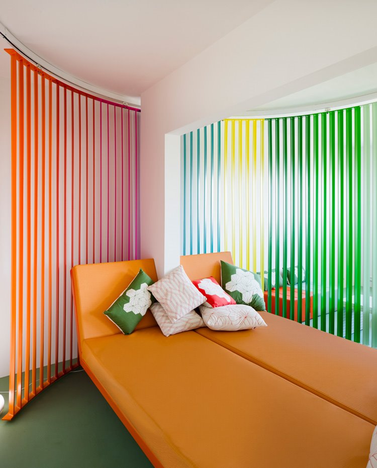 biombo sobre guías corredero multicolor, bancada suspendida en naranja con cojines en rojo, blanco y verde
