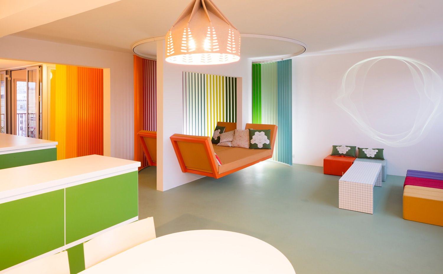 Comedor y sala de estar con sobres en blanco, muebles en verde, bancada en naranja suspendida en pared y pouf de varios colores